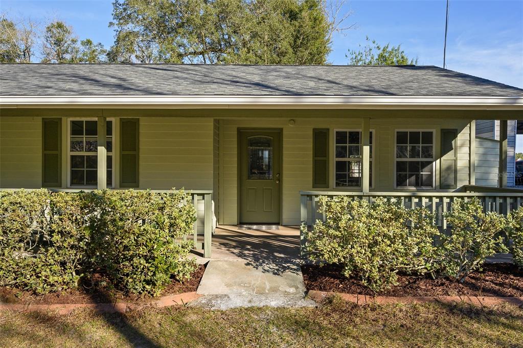 A light green house features a covered front porch with a railing and landscaping — 6878 SW 36TH AVENUE, LAKE BUTLER, FL