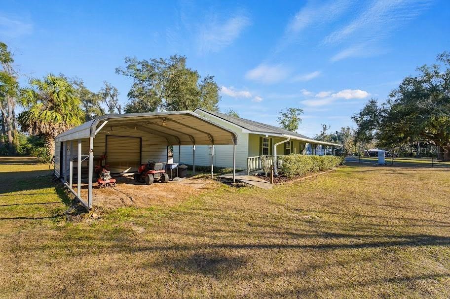 A light-colored house features a large metal carport and a wooden porch in a yard — 6878 SW 36TH AVENUE, LAKE BUTLER, FL