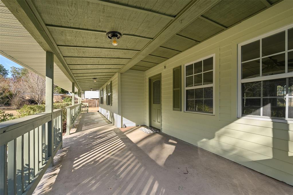 A covered porch with a concrete floor, green siding, and a wooden railing — 6878 SW 36TH AVENUE, LAKE BUTLER, FL
