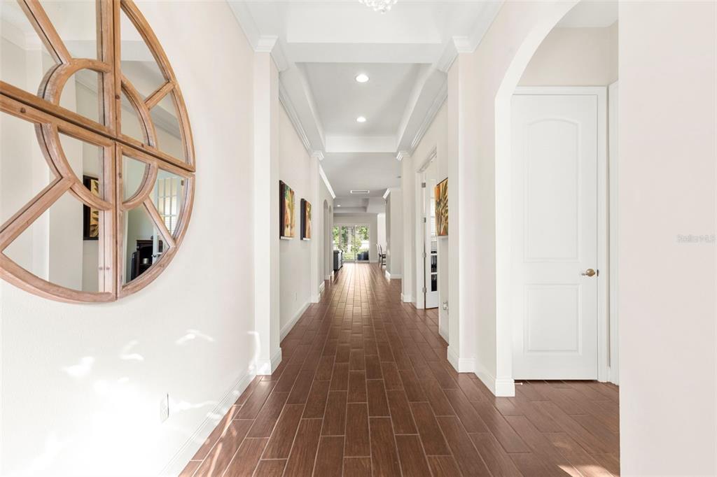 A long hallway with wood-look tile flooring, white walls, and a large circular wall mirror — 5134 LAKECASTLE DRIVE, TAMPA, FL