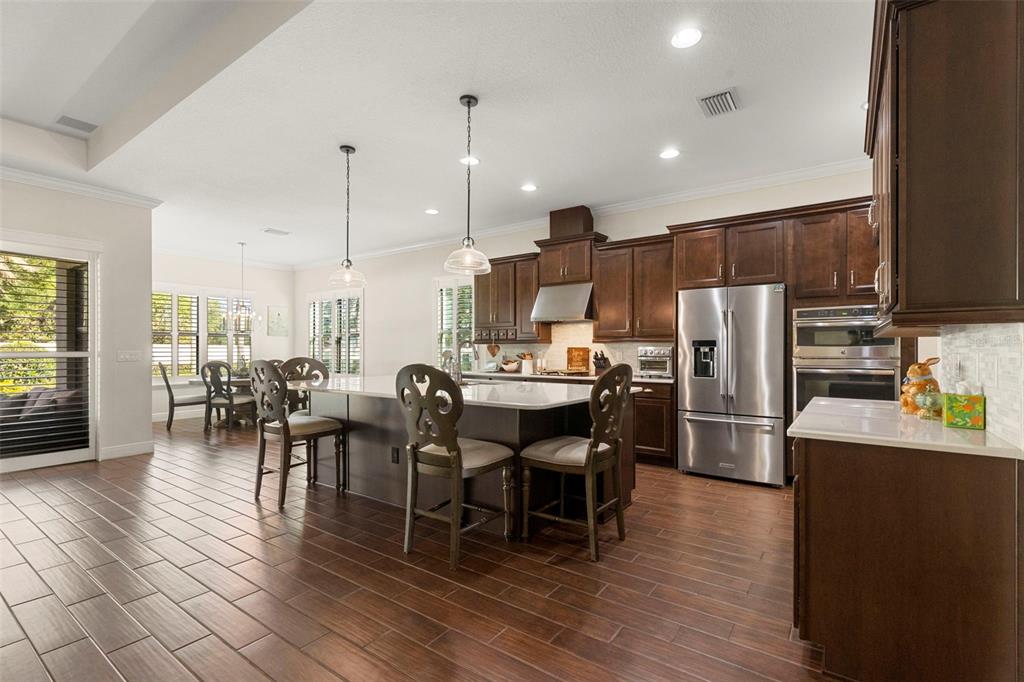 A kitchen features dark wood cabinets, a large island with seating, and wood-look tile flooring — 5134 LAKECASTLE DRIVE, TAMPA, FL