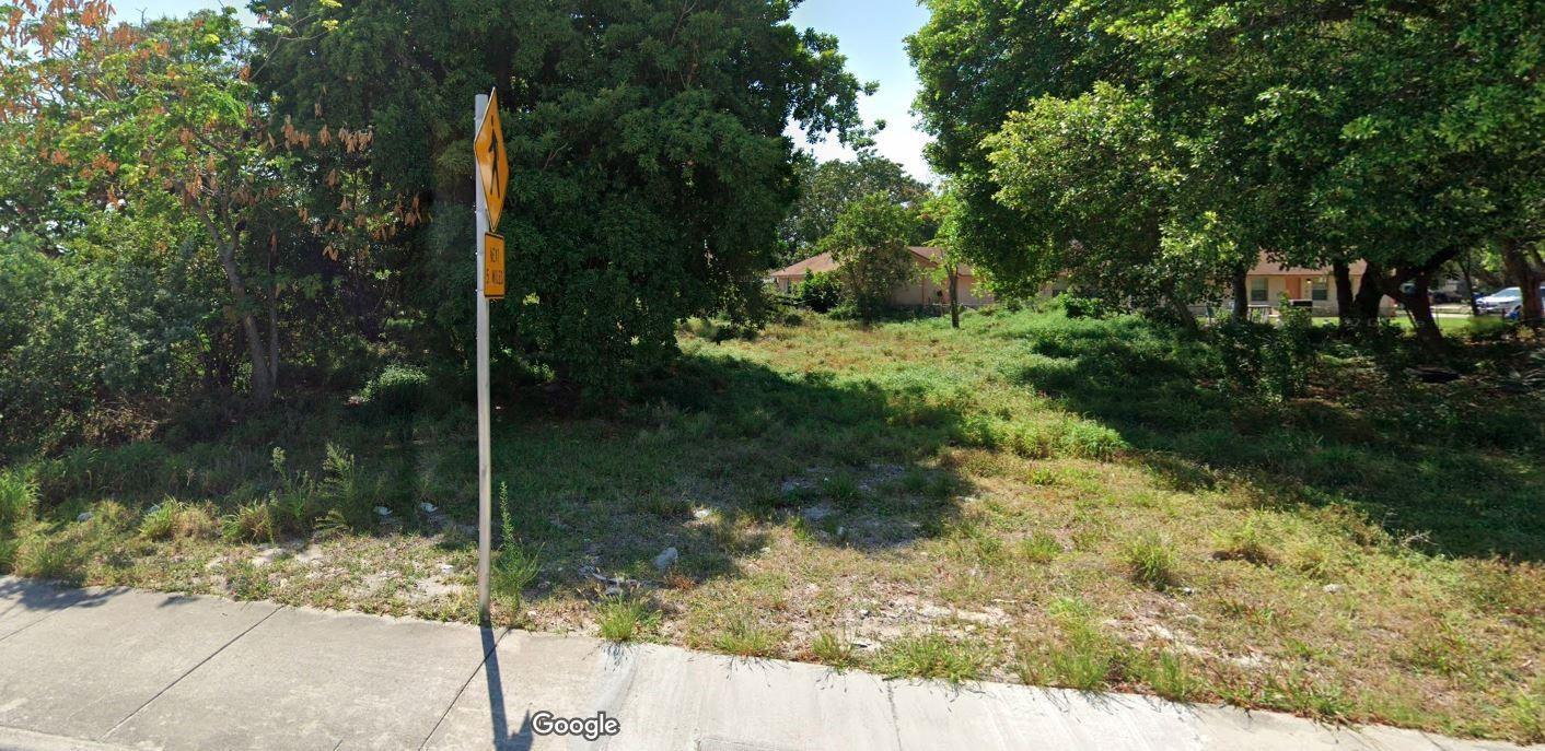 A vacant, grassy lot with mature trees sits next to a sidewalk and a road sign — 583 S Dixie Highway, Deerfield Beach FL 33441, DEERFIELD BEACH, FL