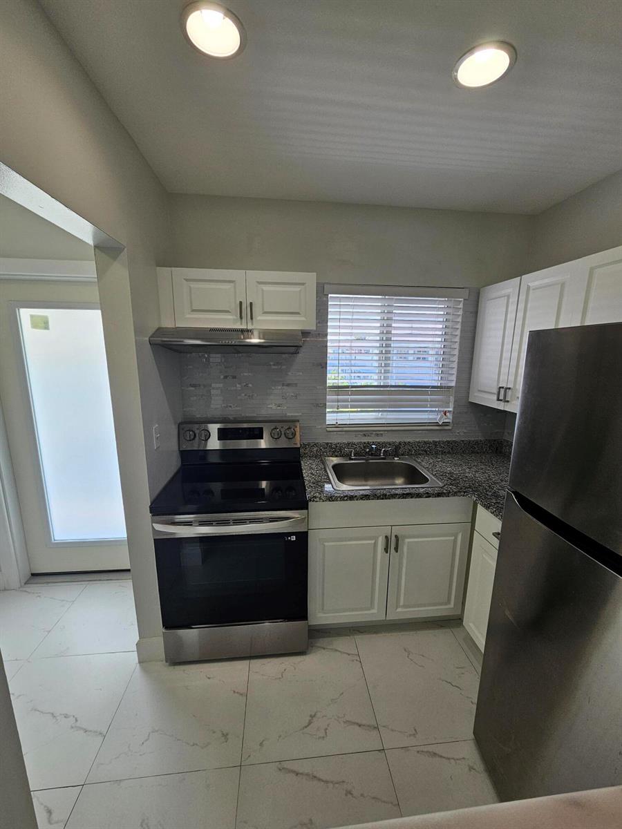 A kitchen features white cabinetry, stainless steel appliances, granite countertops, and light-colored tiled flooring — 1115 Lake Terrace # 208, Boynton Beach FL 33426, BOYNTON BEACH, FL