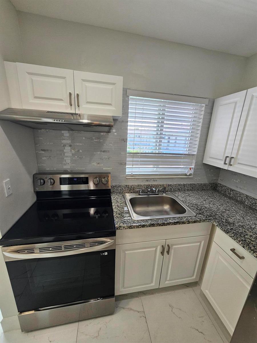 A kitchen features white cabinets, granite countertops, a stainless steel stove, and a sink — 1115 Lake Terrace # 208, Boynton Beach FL 33426, BOYNTON BEACH, FL