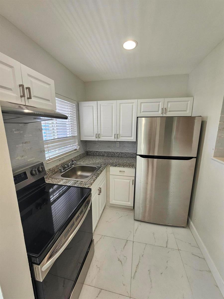 A small kitchen features white cabinets, stainless steel appliances, granite countertops, and light tile flooring — 1115 Lake Terrace # 208, Boynton Beach FL 33426, BOYNTON BEACH, FL