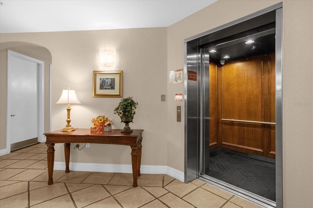 An elevator with wood-paneled walls sits next to a wooden console table in a hallway — 501 MIRASOL CIRCLE UNIT 208, CELEBRATION, FL