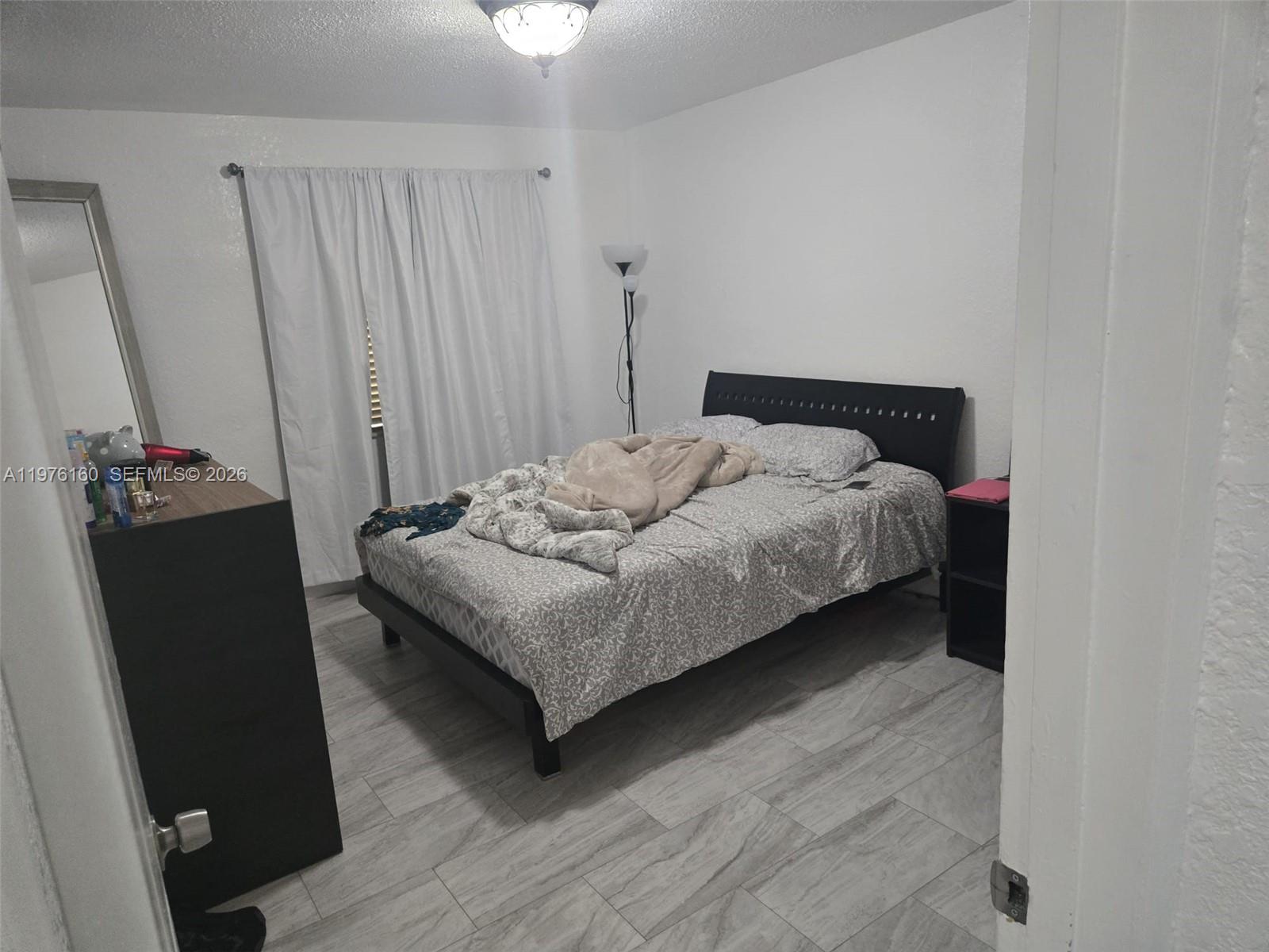 A bedroom features a bed with patterned bedding, a black headboard, and light-colored tile flooring — 1185 W 27th St, Hialeah FL 33010, HIALEAH, FL
