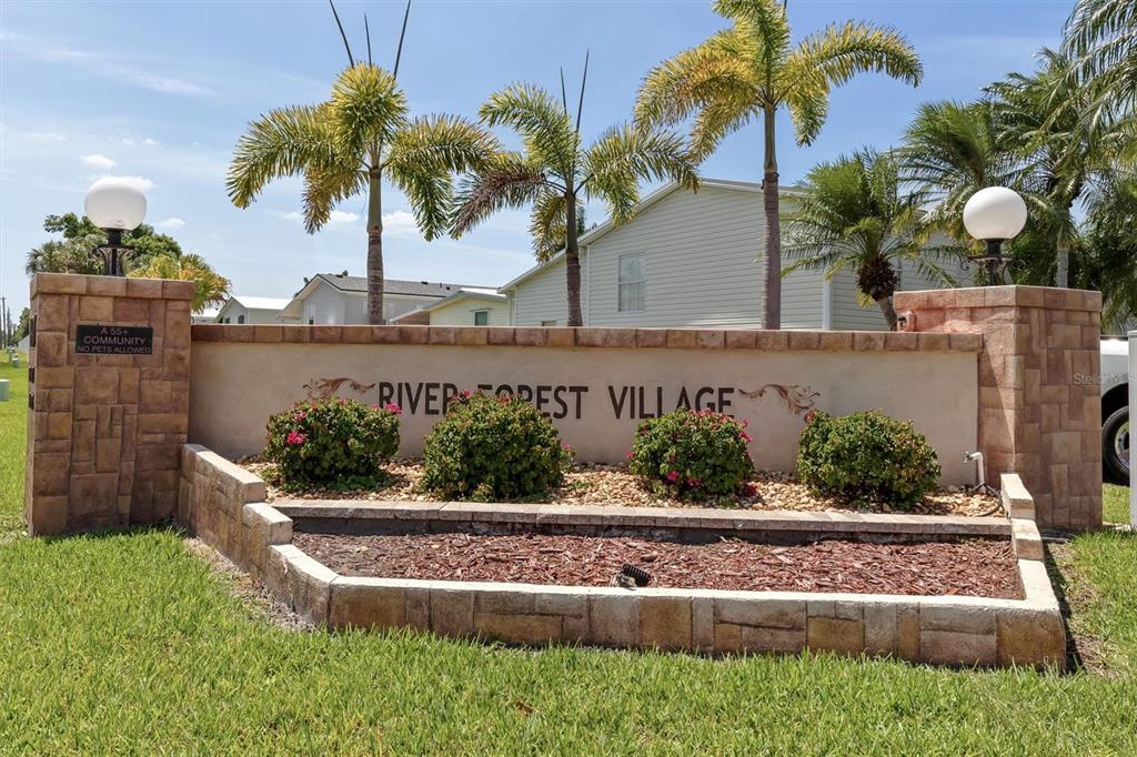The entrance sign for River Forest Village features stone pillars and landscaping under palm trees — 4300 RIVERSIDE DRIVE UNIT 14, PUNTA GORDA, FL