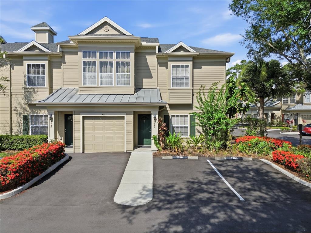 A two-story tan townhouse features a single-car garage, a front walkway, and two parking spaces — 7780 PLANTATION CIRCLE, BRADENTON, FL