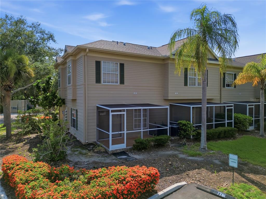 An exterior view of a two-story tan townhouse with a screened-in patio and landscaping — 7780 PLANTATION CIRCLE, BRADENTON, FL