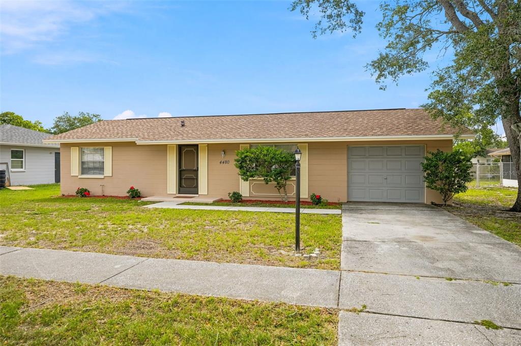 A single-story tan house with a brown shingled roof, a garage, and a front lawn — 4480 BROMLEY AVENUE, SPRING HILL, FL