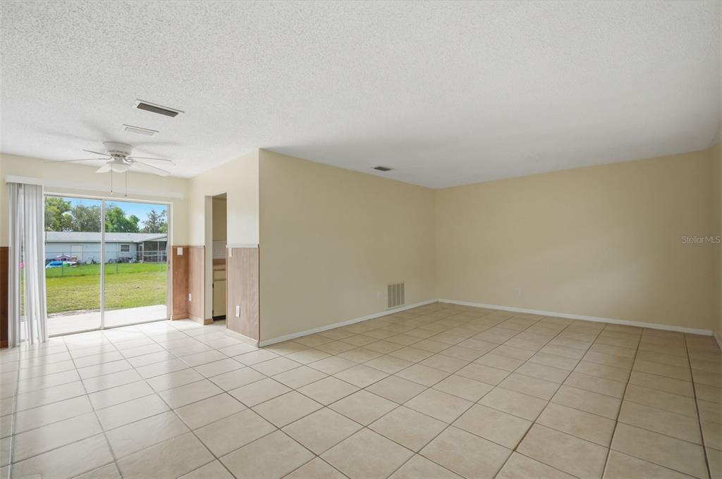 An empty room with beige tile flooring, a ceiling fan, and sliding glass patio doors — 4480 BROMLEY AVENUE, SPRING HILL, FL