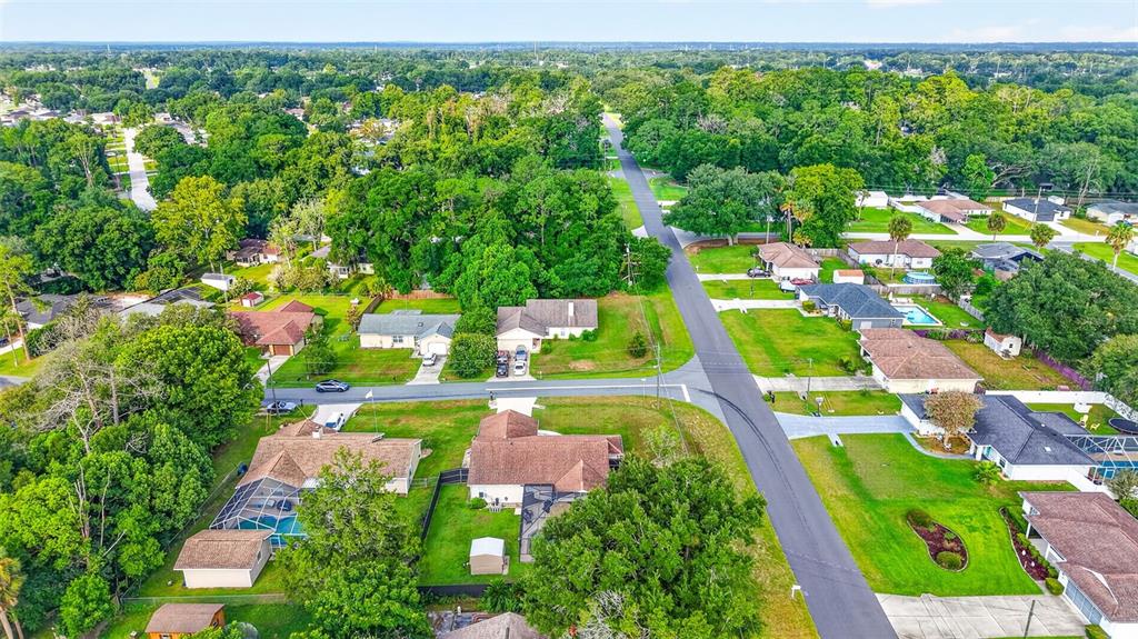 An aerial view shows suburban houses with swimming pools surrounded by dense green trees — 1 TEAK COURT, OCALA, FL