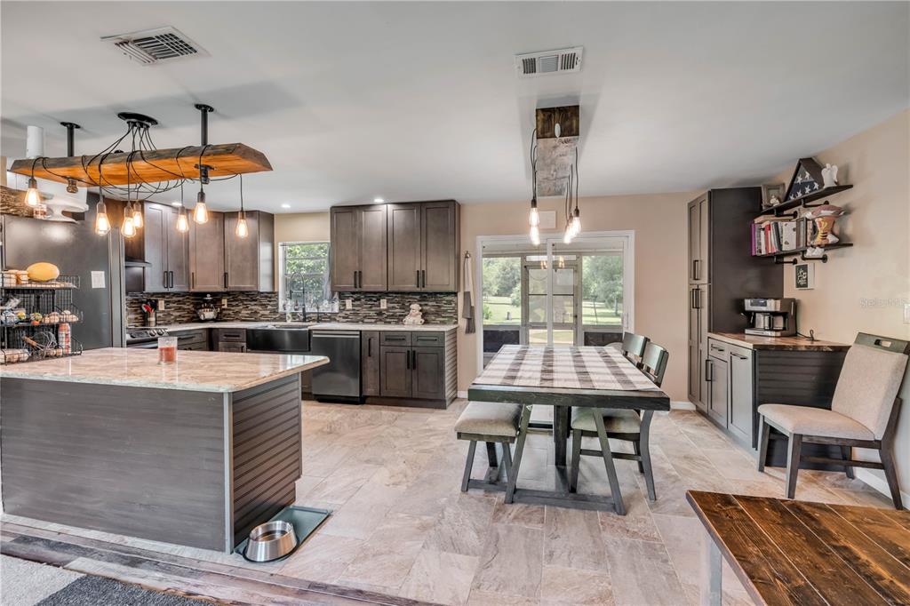 A kitchen features dark cabinetry, a stone-topped island, tile flooring, and a dining area — 1167 OHIO STREET, DE LEON SPRINGS, FL