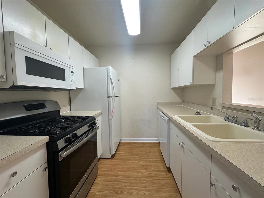 A galley-style kitchen features white cabinets, a black gas range, and a white refrigerator — 2050 SAN MARCOS DRIVE SE UNIT 214, WINTER HAVEN, FL