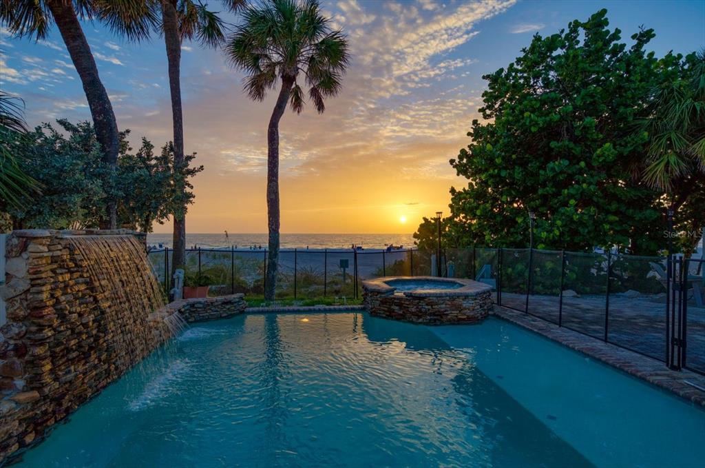 A swimming pool with a stone waterfall and hot tub overlooks a beach at sunset — 2308 BEACH TRAIL, INDIAN ROCKS BEACH, FL