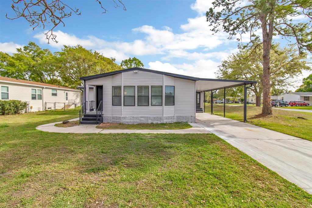 A single-story manufactured home with light gray siding, a front porch, and an attached carport — 217 ELLSWORTH DRIVE, KISSIMMEE, FL