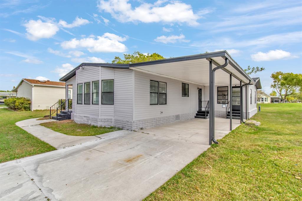 A light gray manufactured home with a concrete driveway and an attached metal carport — 217 ELLSWORTH DRIVE, KISSIMMEE, FL