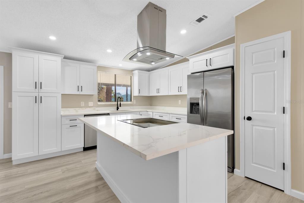 A modern kitchen features white cabinets, a quartz-topped island, stainless steel appliances, and light flooring — 217 ELLSWORTH DRIVE, KISSIMMEE, FL