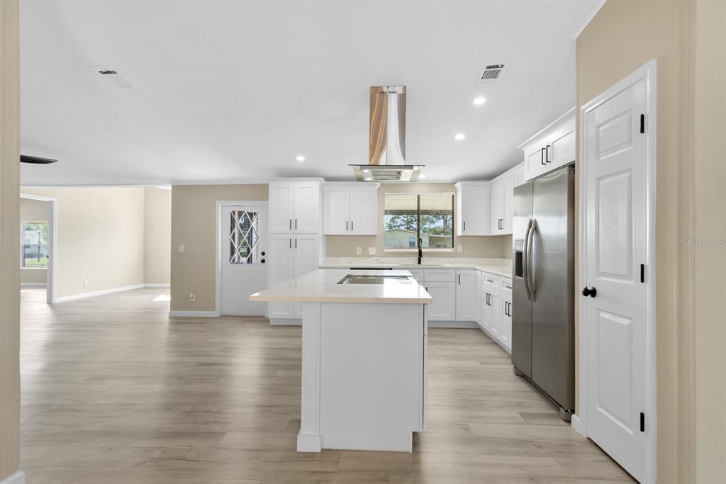 A modern kitchen features white cabinets, a central island, stainless steel appliances, and wood flooring — 217 ELLSWORTH DRIVE, KISSIMMEE, FL