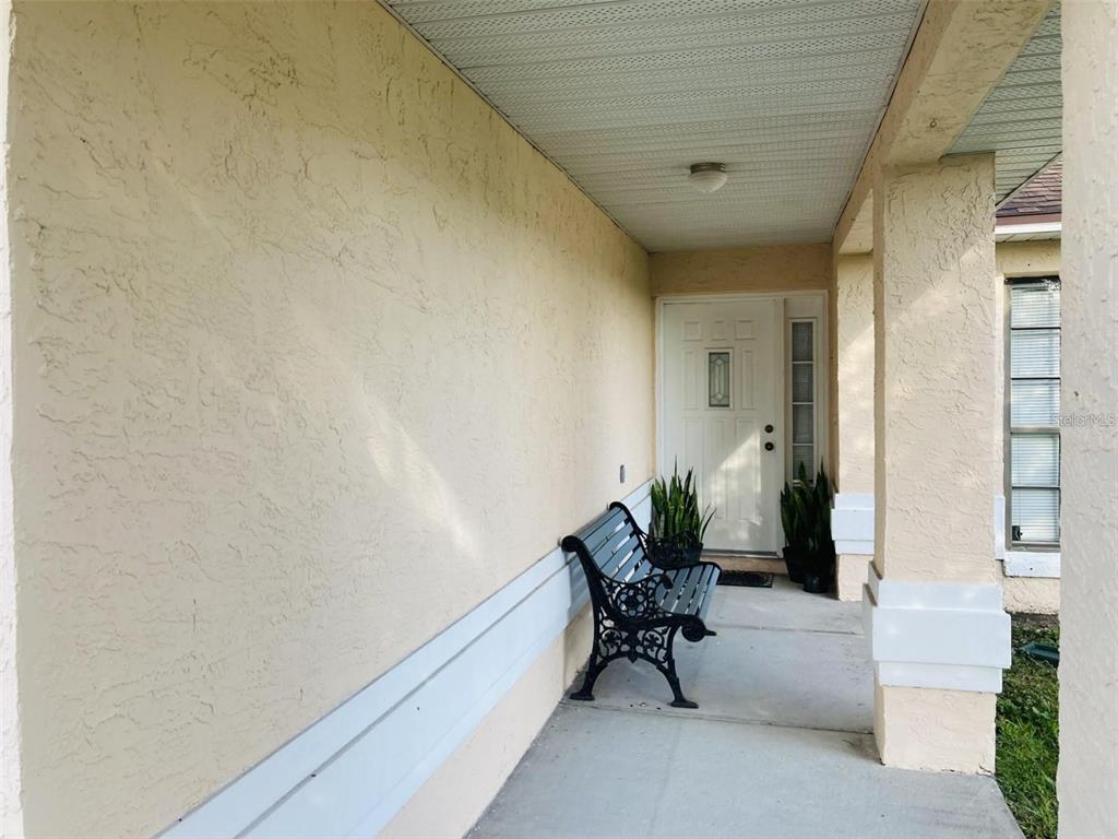 A covered front porch features a black metal bench, potted plants, and a white door — 2704 KENDALL AVENUE, KISSIMMEE, FL