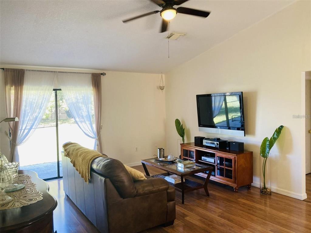 A living room features a leather sofa, a wooden media console, and sliding glass doors — 2704 KENDALL AVENUE, KISSIMMEE, FL