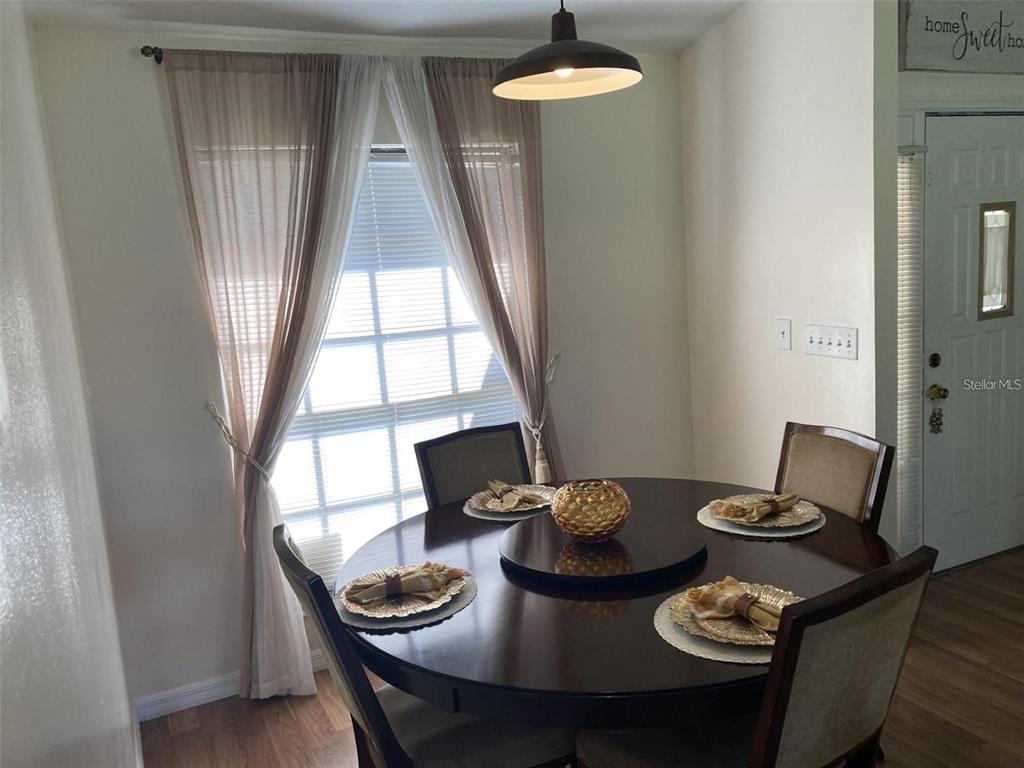 A dining room features a round wooden table, four chairs, and a window with curtains — 2704 KENDALL AVENUE, KISSIMMEE, FL