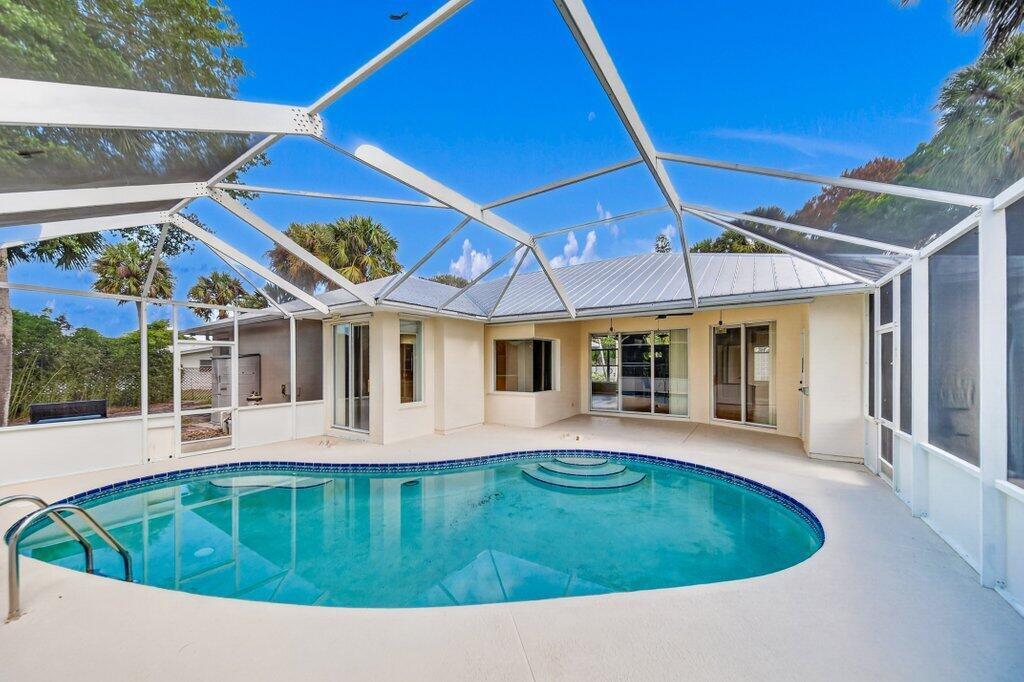 A swimming pool with a screened-in enclosure sits on a patio behind a residential house — 612 SE 6th Street, Stuart FL 34994, STUART, FL