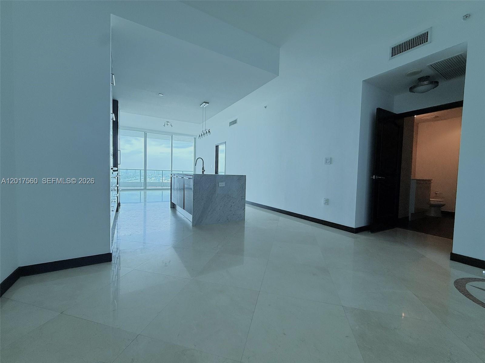 A modern kitchen with a marble island and light tile floors overlooks a city view — 900 Biscayne Blvd # 3803, Miami FL 33132, MIAMI, FL