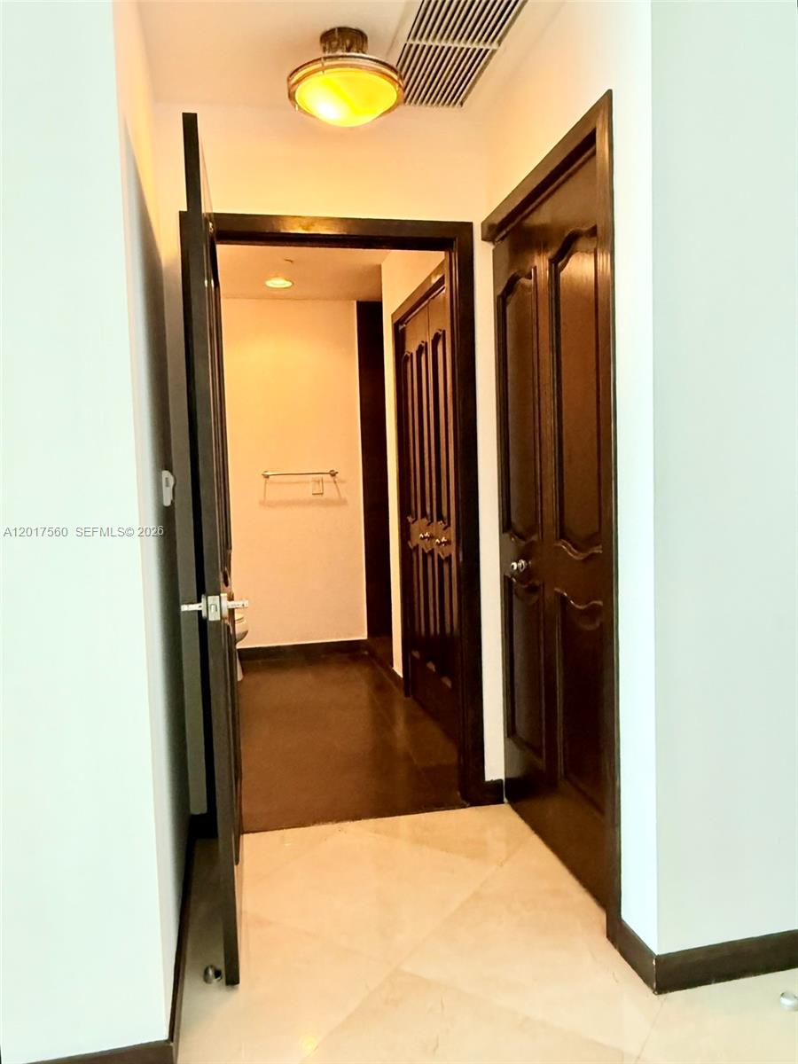 A hallway leads to a bathroom with dark wood doors and light-colored tile flooring — 900 Biscayne Blvd # 3803, Miami FL 33132, MIAMI, FL
