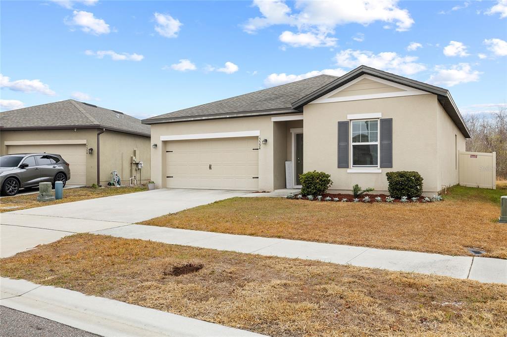 A single-story suburban house with a beige stucco exterior, a two-car garage, and a lawn — 5534 TURKEY CREEK WAY, LAKELAND, FL