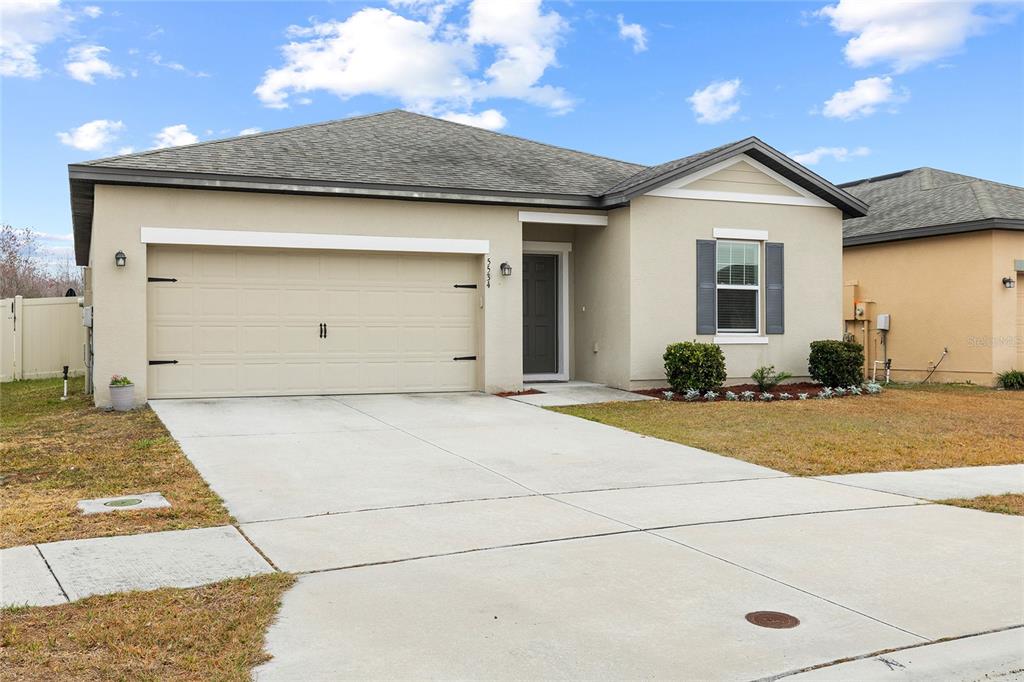 A single-story house with a beige stucco exterior, a two-car garage, and a concrete driveway — 5534 TURKEY CREEK WAY, LAKELAND, FL