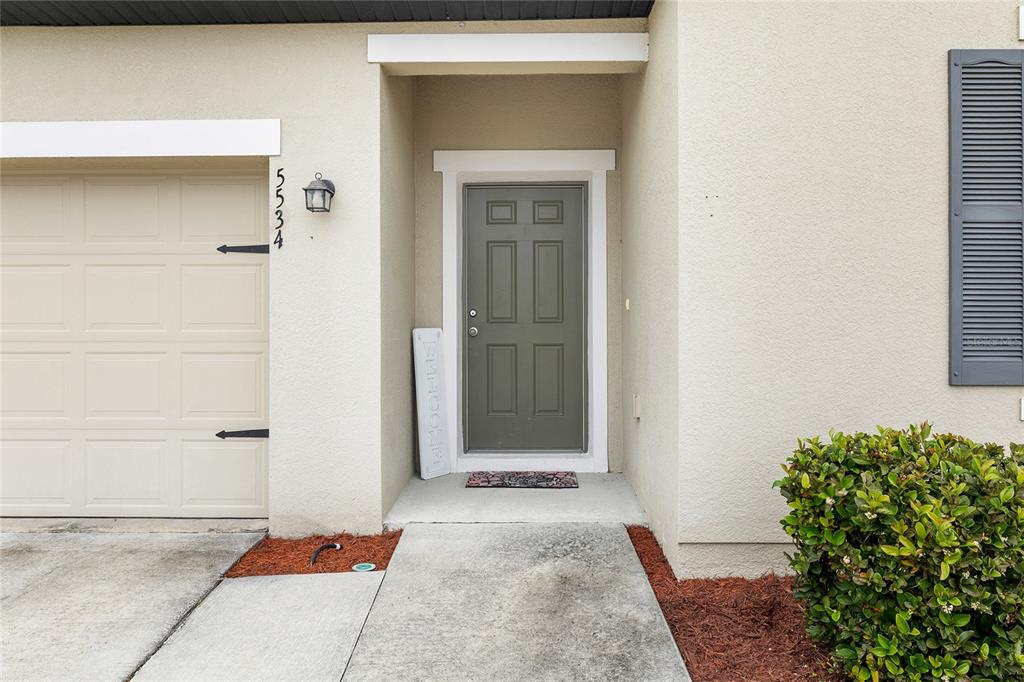 A tan house exterior features a gray front door, a garage, and a small bush — 5534 TURKEY CREEK WAY, LAKELAND, FL