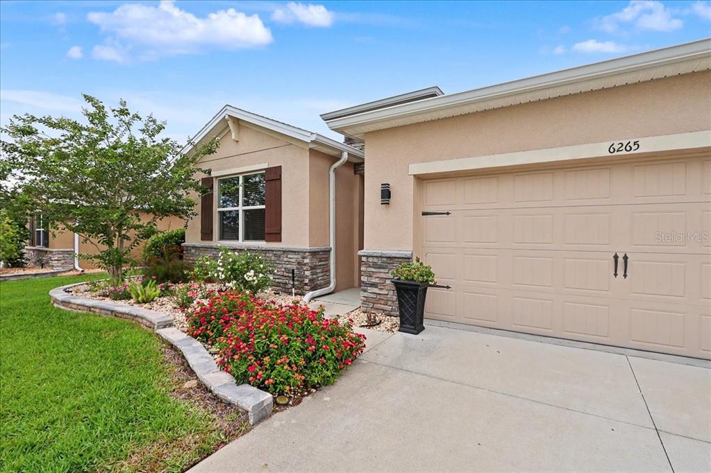 A tan stucco house features a stone-accented garage, a front garden, and brown shutters — 6265 SW 88 LOOP, OCALA, FL