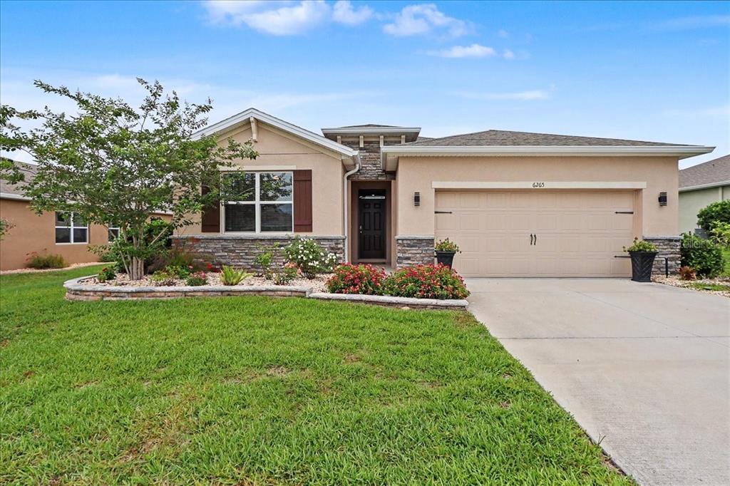 A single-story house with a beige stucco exterior, stone accents, and a two-car garage — 6265 SW 88 LOOP, OCALA, FL