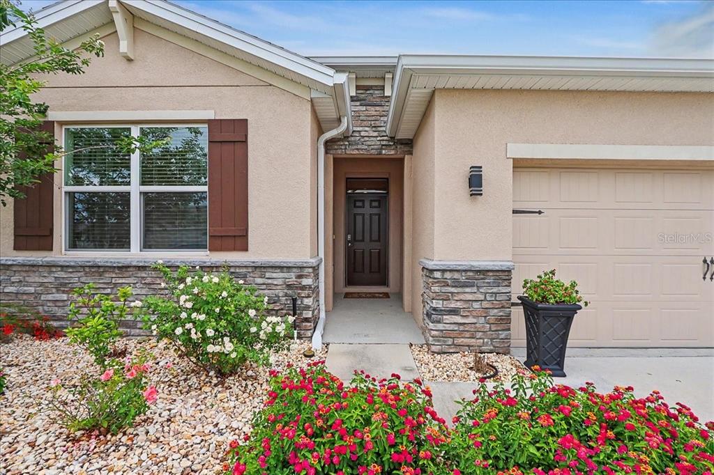 The exterior of a single-story house features a stone facade, a garage, and landscaped flowerbeds — 6265 SW 88 LOOP, OCALA, FL