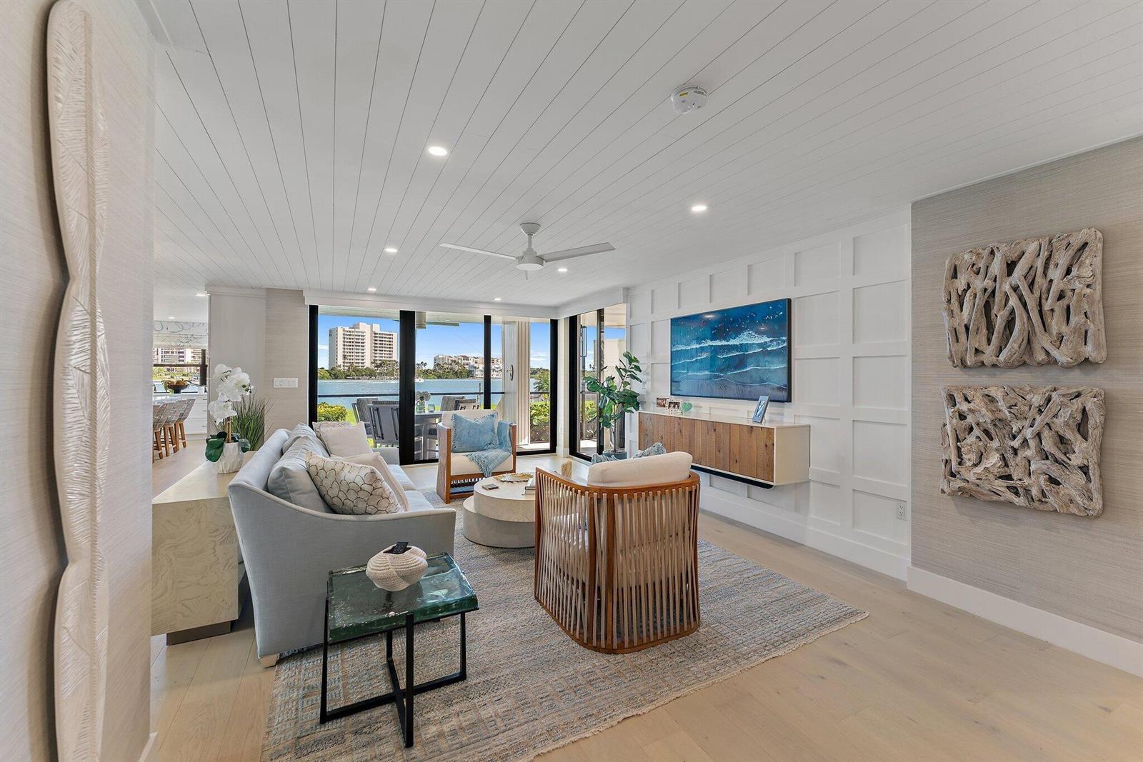 A living room features a white paneled wall, a floating media console, and waterfront views — 19800 Sandpointe Bay Drive # 101, Tequesta FL 33469, TEQUESTA, FL