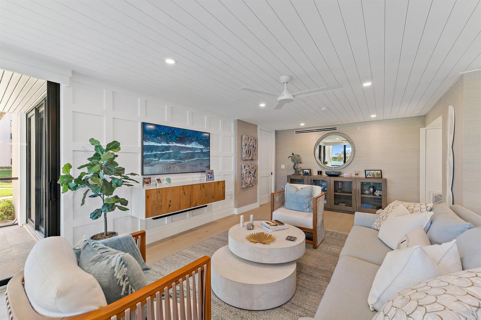 A bright living room features white paneled walls, a wood floating console, and coastal decor — 19800 Sandpointe Bay Drive # 101, Tequesta FL 33469, TEQUESTA, FL
