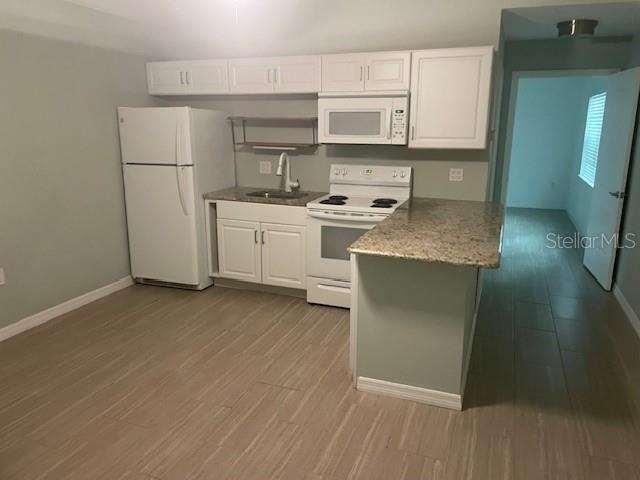 A kitchen features white cabinetry, a white refrigerator, a stove, and a granite countertop — 1610 HAVEN DRIVE UNIT Rear, ORLANDO, FL