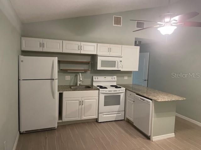 A kitchen features white cabinets, white appliances, and a granite countertop peninsula — 1610 HAVEN DRIVE UNIT Rear, ORLANDO, FL