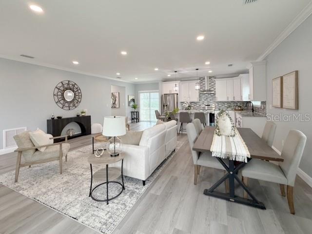 An open-concept living and dining area features light wood flooring, white cabinetry, and neutral furniture — 1083 S POINTE ALEXIS DRIVE, TARPON SPRINGS, FL