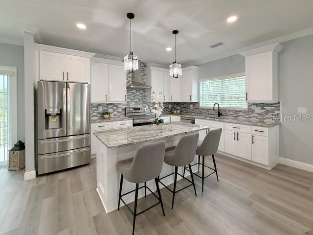 A modern kitchen features white cabinets, a stone-topped island with gray stools, and stainless appliances — 1083 S POINTE ALEXIS DRIVE, TARPON SPRINGS, FL