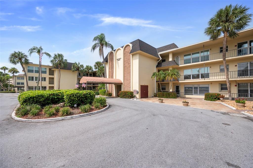 The exterior of a multi-story apartment building features a covered entrance and palm trees — 4780 COVE CIRCLE STREET UNIT 103, ST PETERSBURG, FL