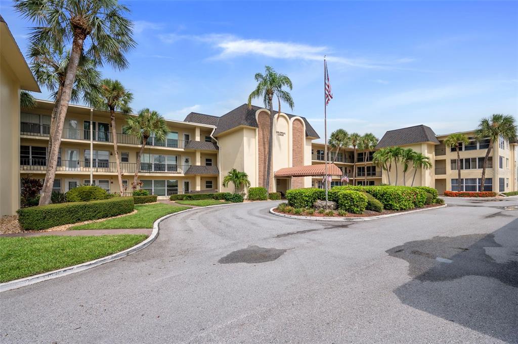 A multi-story apartment building with a circular driveway, palm trees, and a central entrance canopy — 4780 COVE CIRCLE STREET UNIT 103, ST PETERSBURG, FL