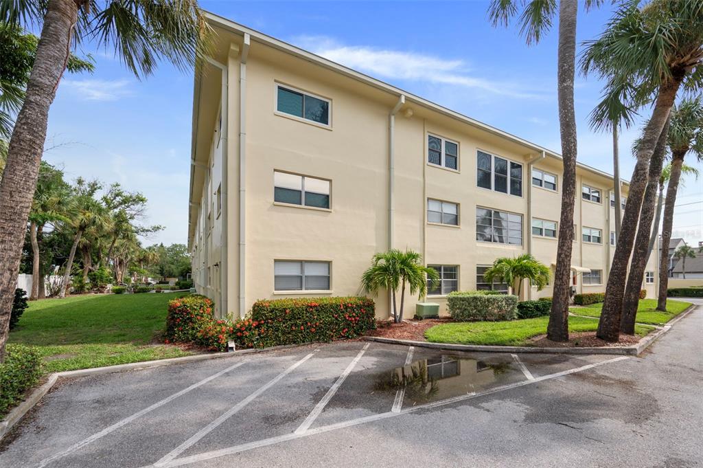 A three-story apartment building with beige stucco walls sits next to a parking lot — 4780 COVE CIRCLE STREET UNIT 103, ST PETERSBURG, FL