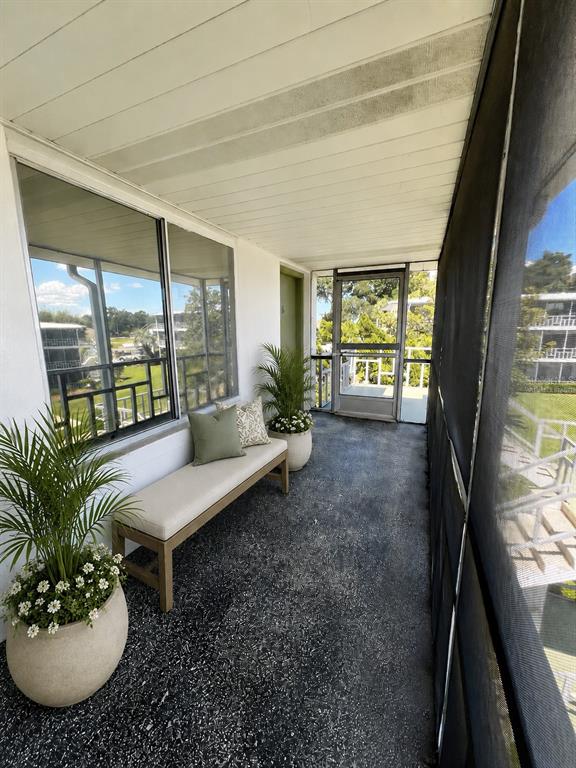 A screened-in balcony features a bench, potted plants, and views of a neighboring building — 1700 6TH STREET NW UNIT A38, WINTER HAVEN, FL