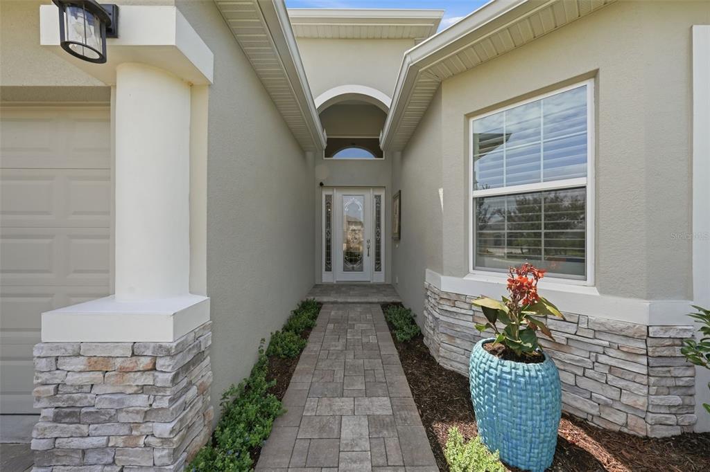 A stone-accented entryway features a paved walkway leading to a glass-paneled front door — 8732 PROVIDENCE COURT, MOUNT DORA, FL