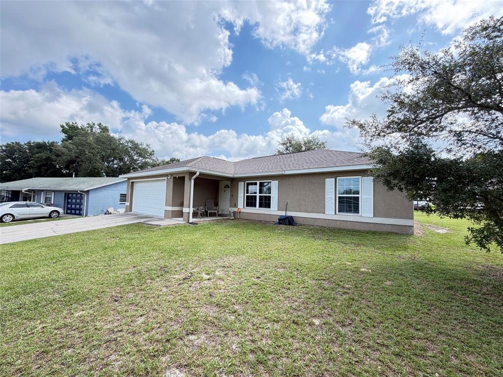 A single-story tan stucco house with a white garage door and a grassy front yard — 3737 SW 150TH LOOP, OCALA, FL