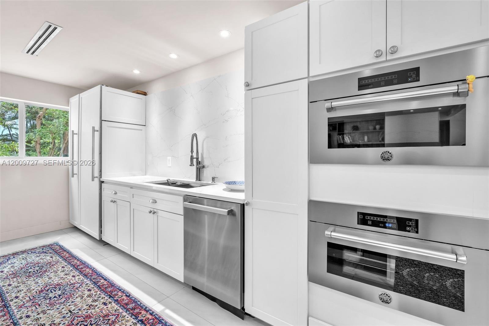 A modern kitchen features white cabinetry, stainless steel appliances, and a marble-patterned backsplash — 1933 S Oak Haven Cir, Miami FL 33179, MIAMI, FL