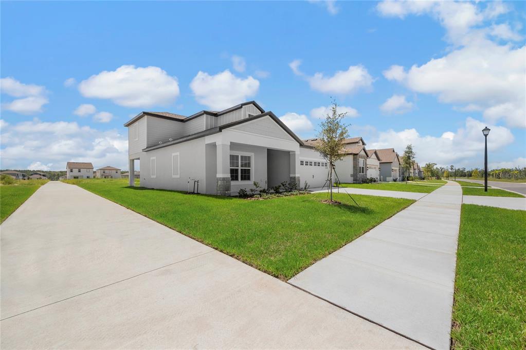A modern, light-gray single-family home with a concrete driveway and sidewalk under a blue sky — 3384 CHINOTTO DRIVE, LAKE ALFRED, FL